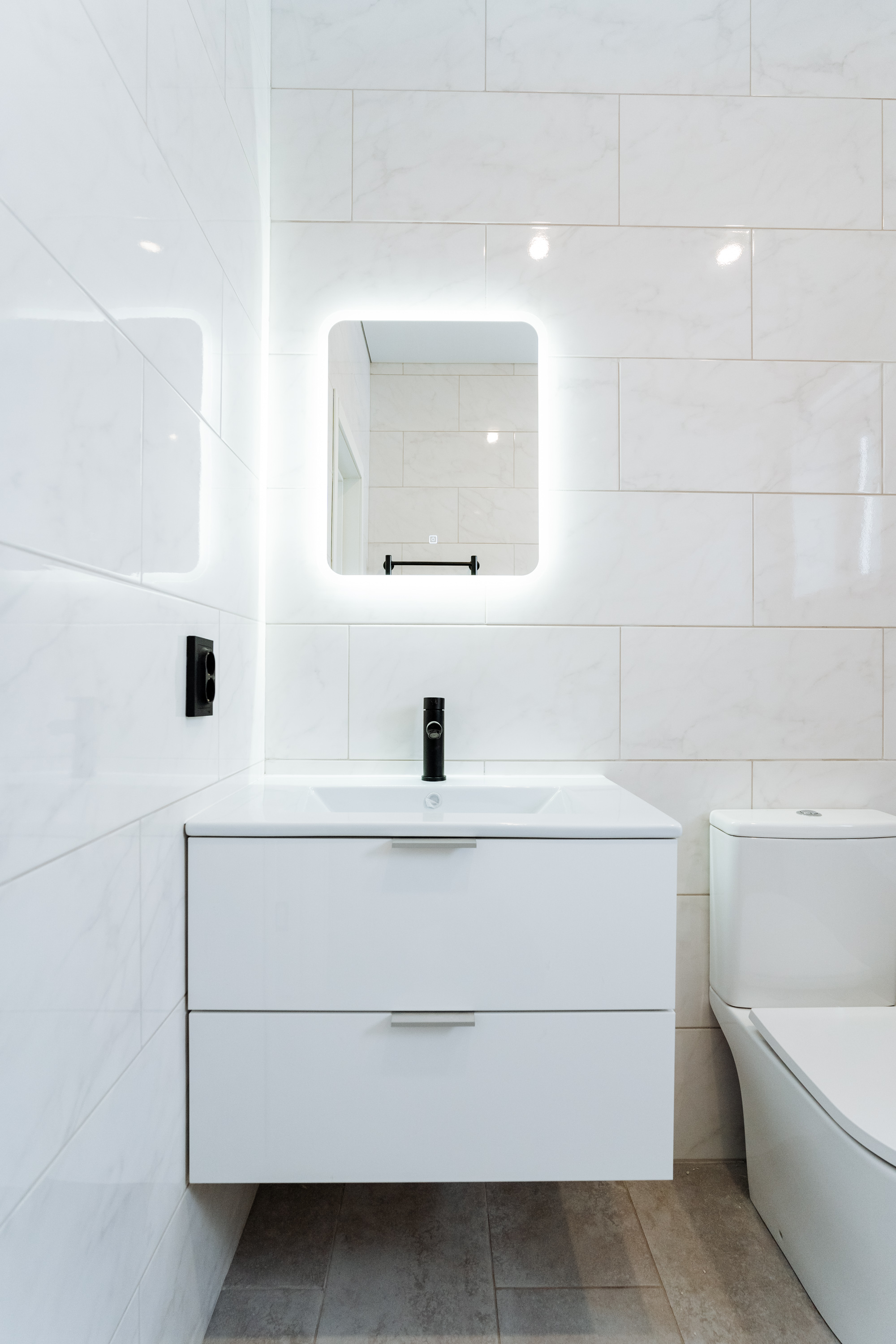 Minimalist white bathroom with backlit mirror and floating vanity